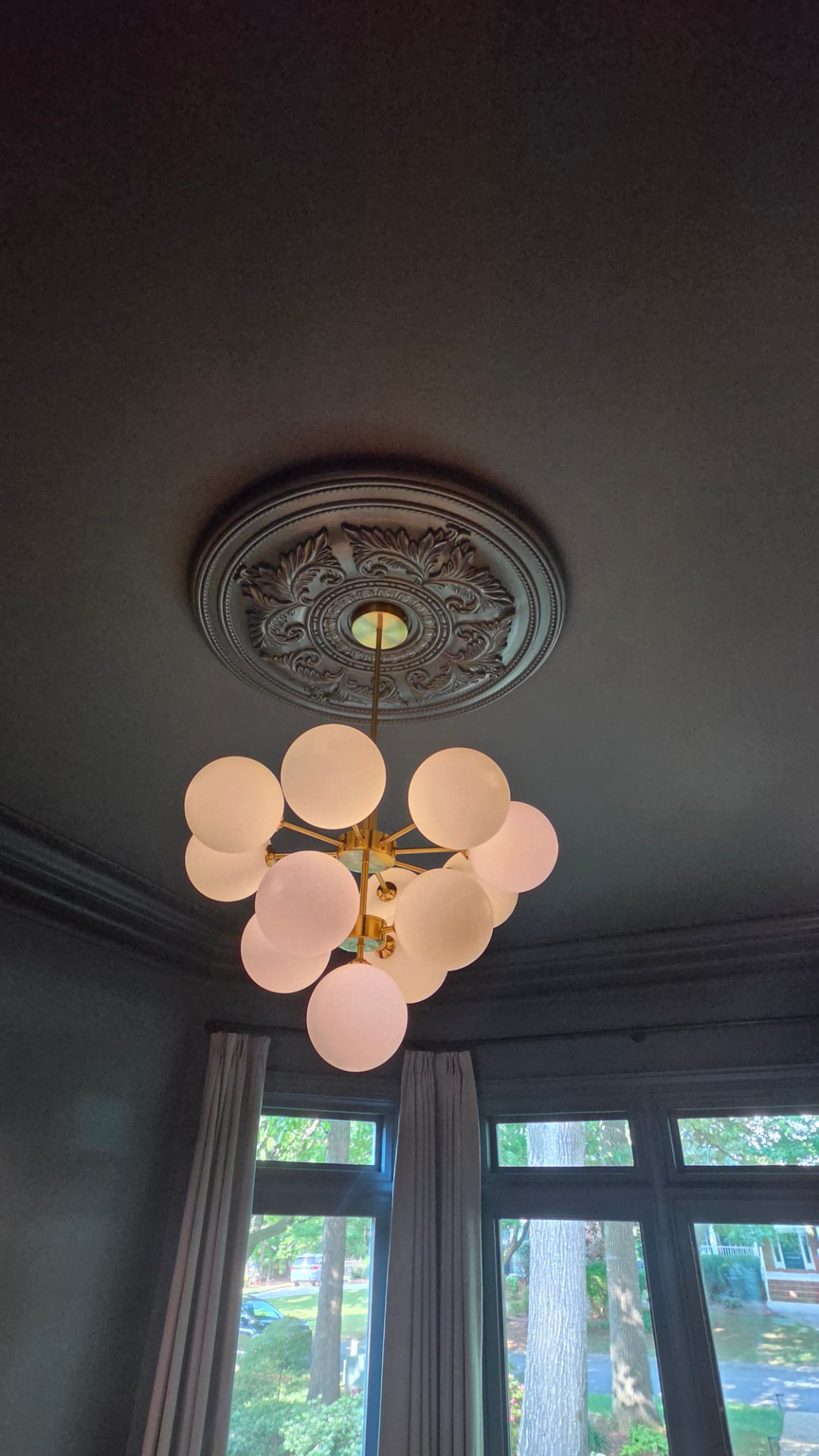 Ornate ceiling medallion and brass sputnik chandelier above the bay window, all painted the same deep slate green