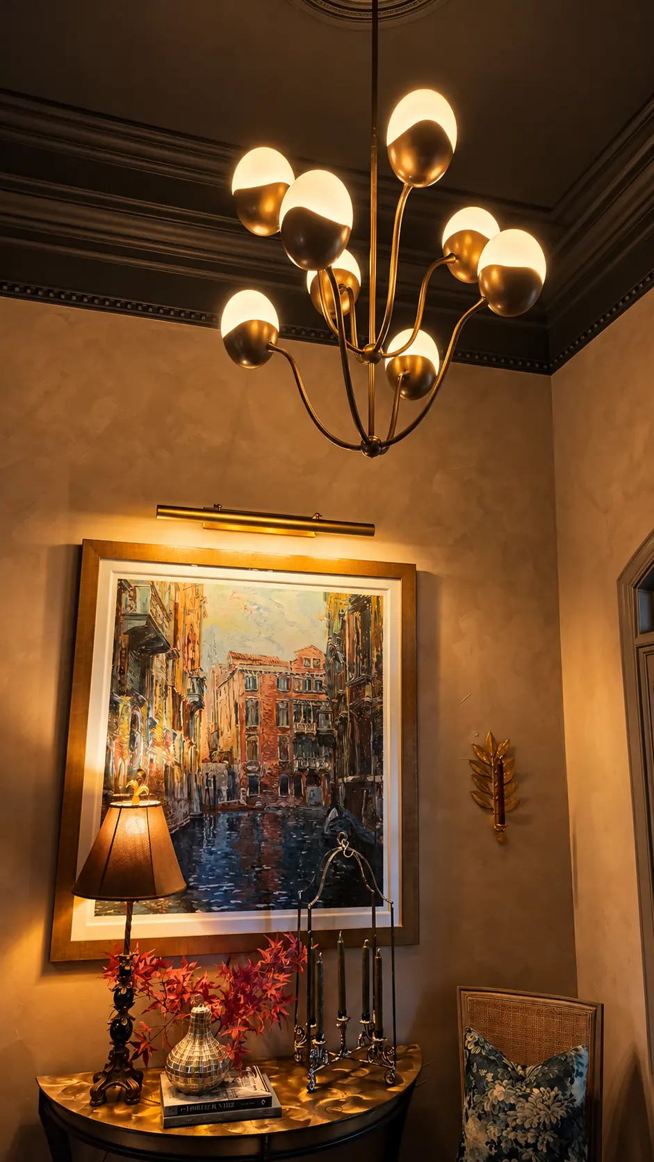Close view of the sculptural brass Primrose chandelier against the dark ceiling, above the illuminated artwork and seasonal red foliage