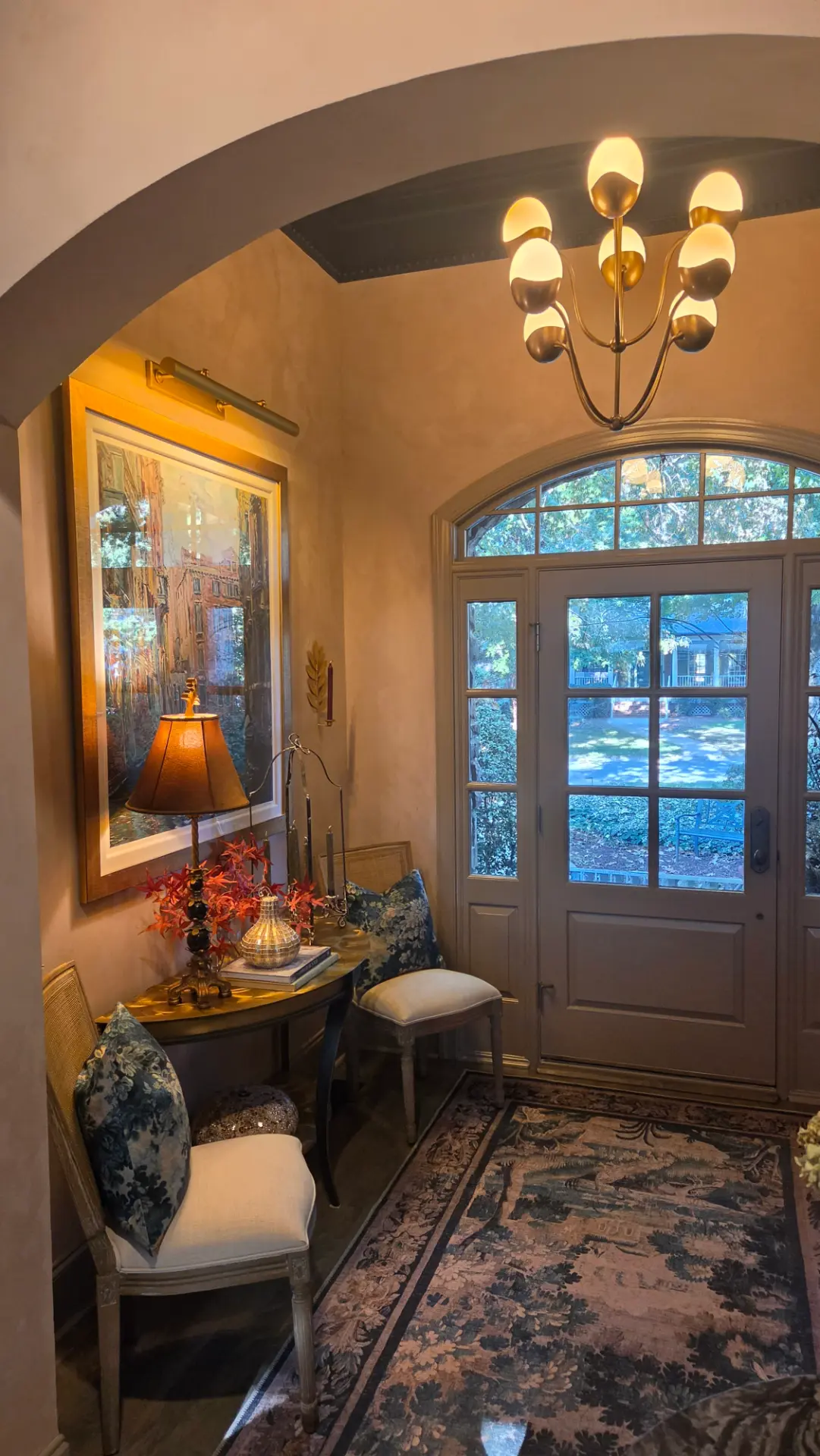 View through an arch toward the glazed front door, patterned blue rug, cane chairs and illuminated Venice artwork