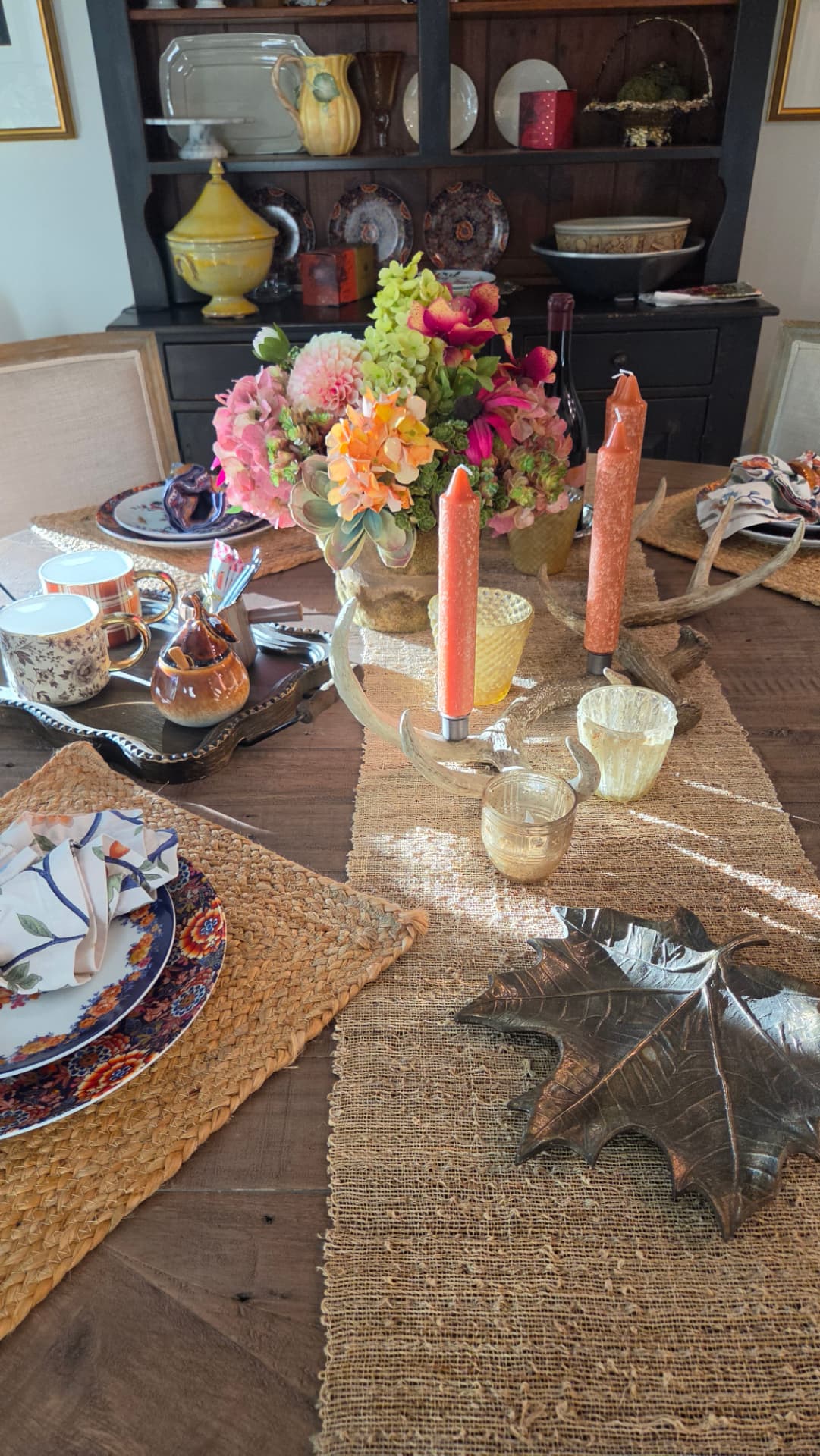 A fall dining table set with antler candle holders, rattan chargers and autumn florals in morning light