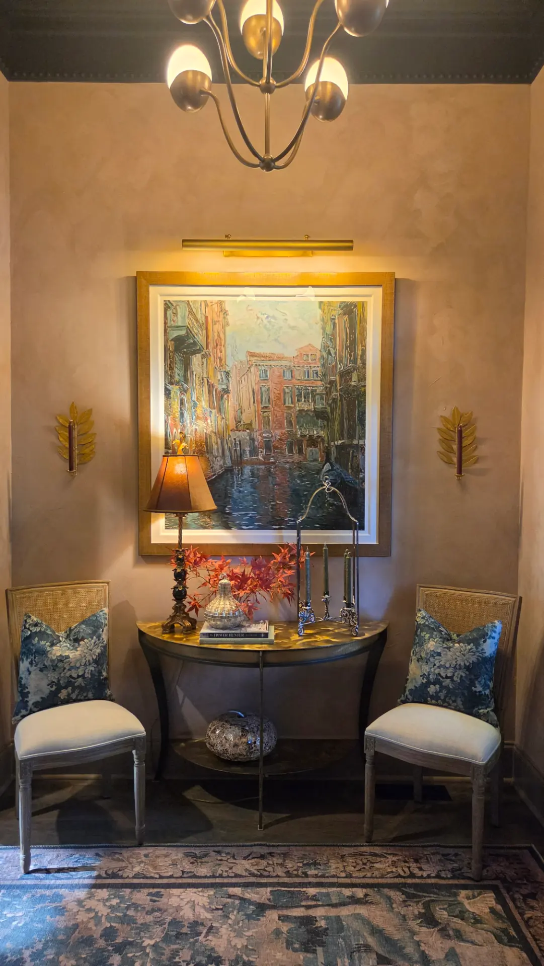 Marco Sassone's Venice serigraph under a brass picture light, above a console flanked by cane chairs and floral blue cushions