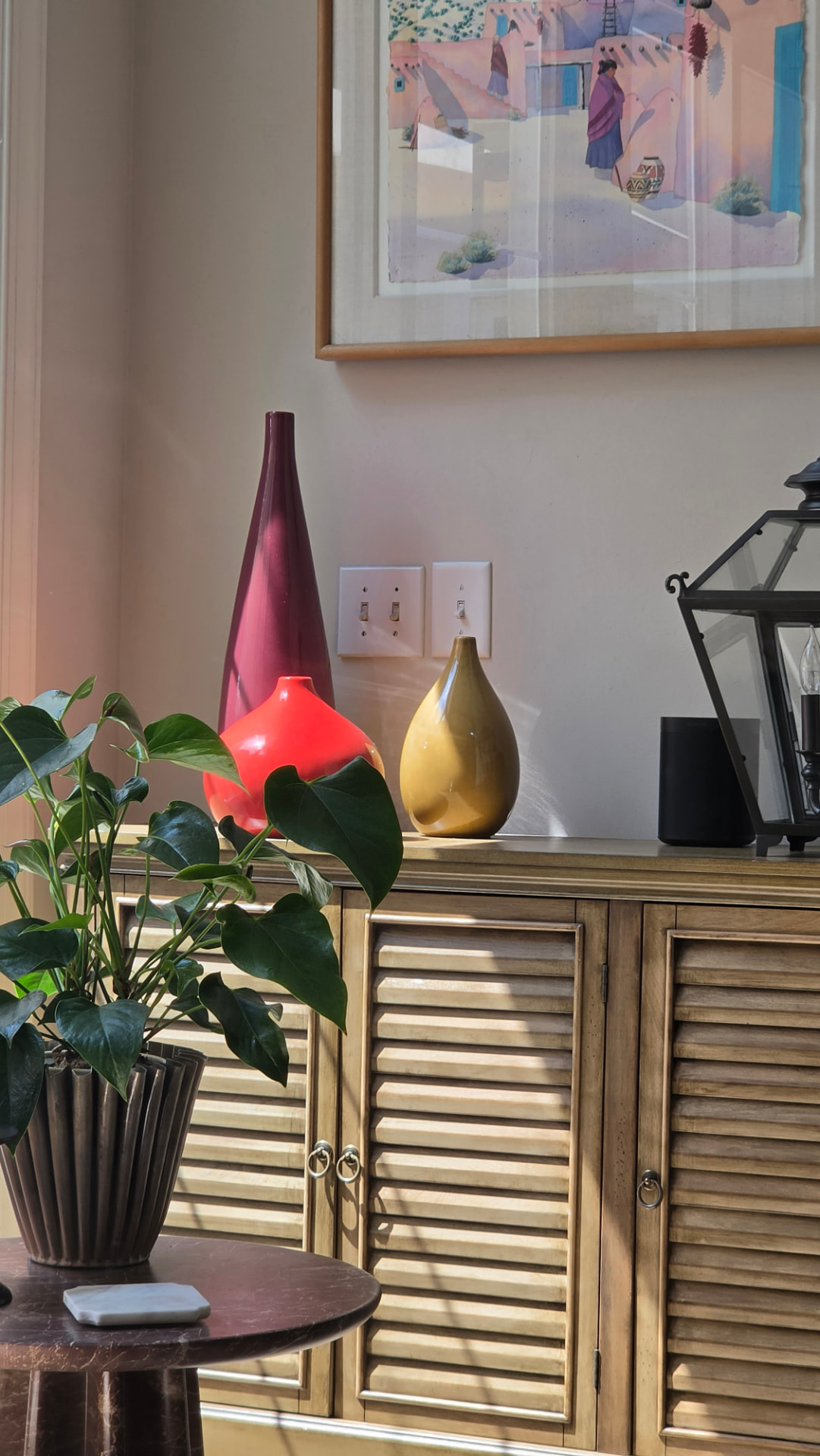 Low winter sun raking across a sideboard with plum, red and ochre vases and a leafy plant