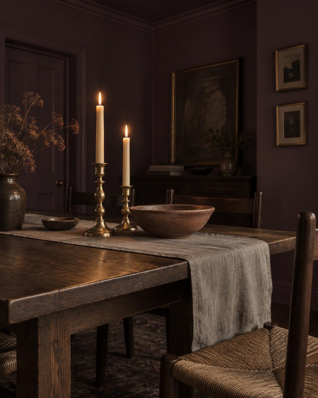Brass candlesticks and a terracotta bowl on the oak table under candlelight in the plum dining room