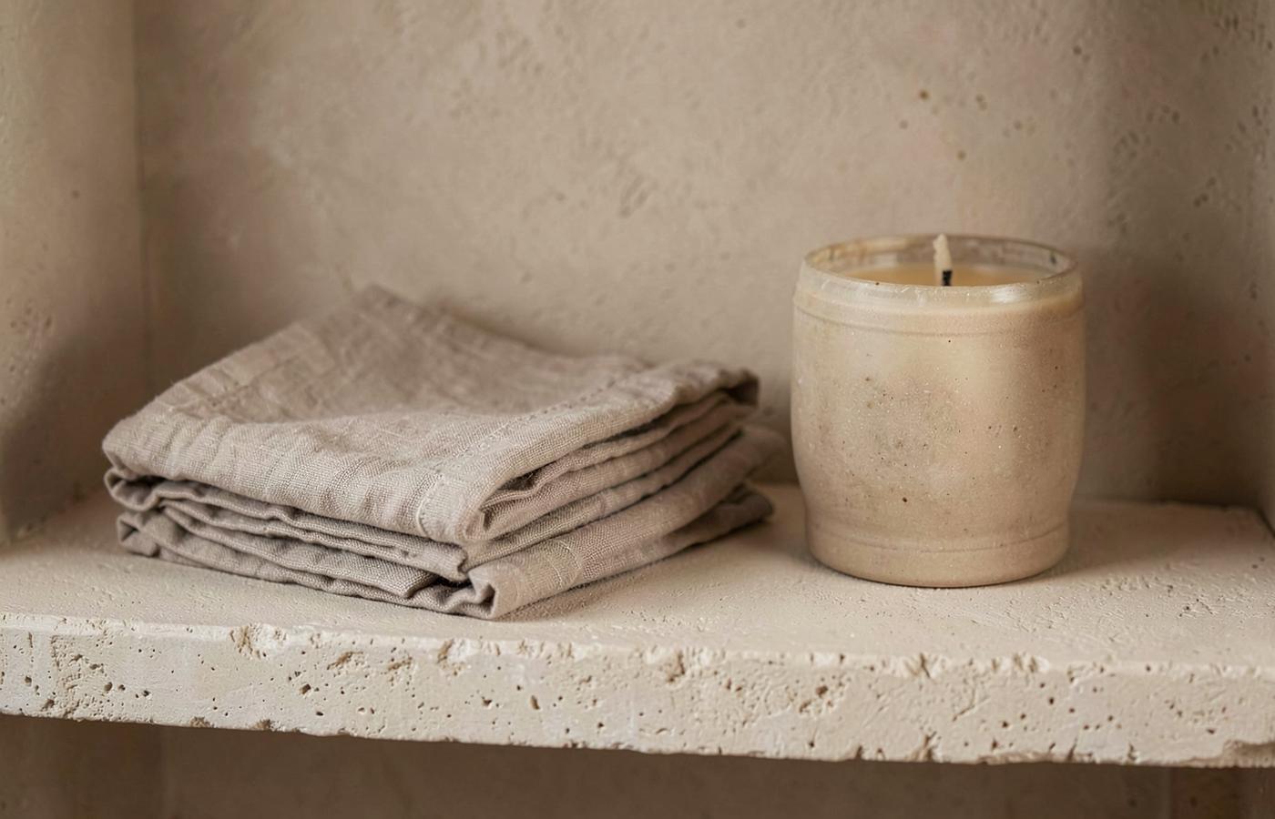 Linen napkins and a stoneware candle on a plaster shelf